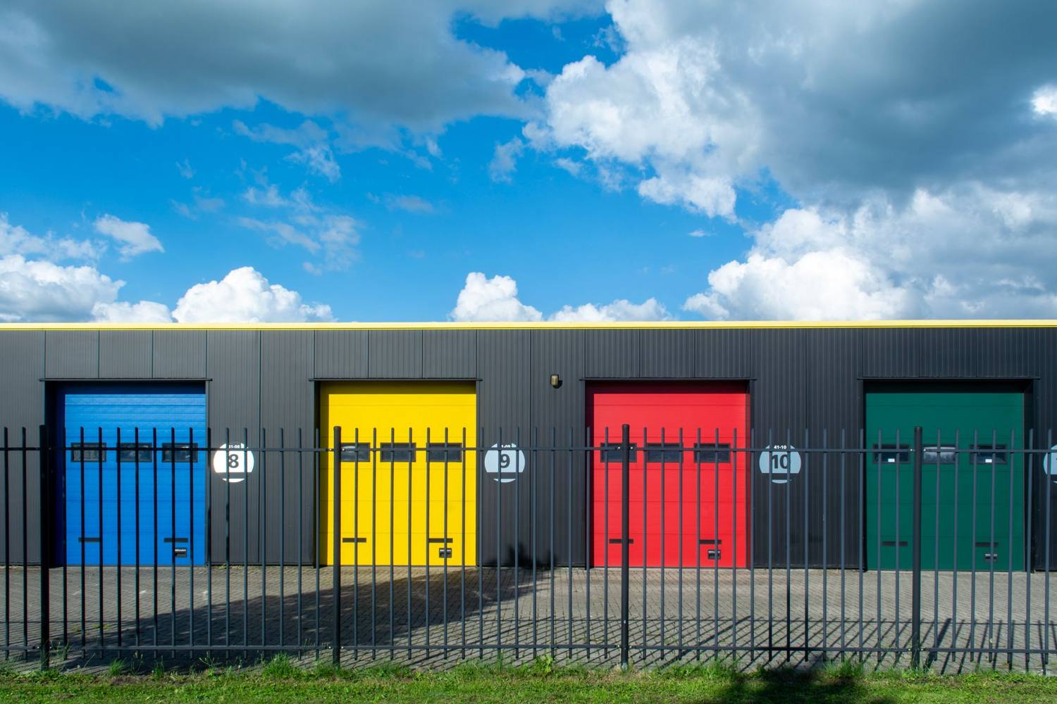 Des portes de garage vibrantes à des couleurs primaires contrastent avec un ciel bleu brillant. Style industriel moderne.